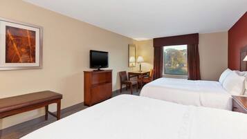 Een hotelkamer met twee bedden, een bureau met stoel, een televisie en een raam met gordijnen.