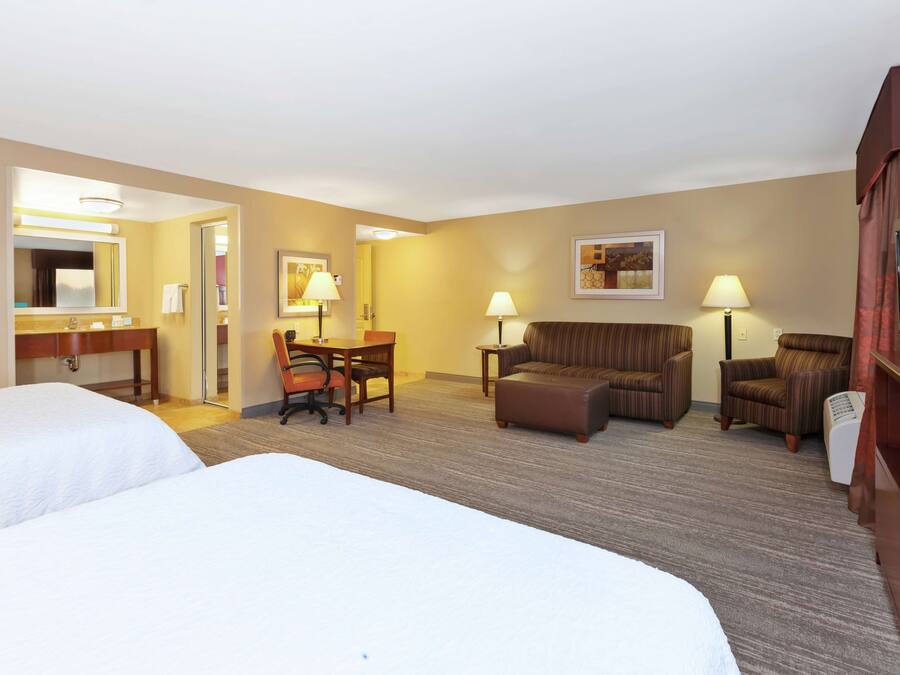 A hotel room with two beds, a desk with a chair, a sofa, two armchairs, a TV, and a lamp.