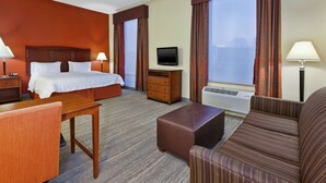 Habitación de hotel con cama, televisión, escritorio, silla, sofá y ventana con cortinas.