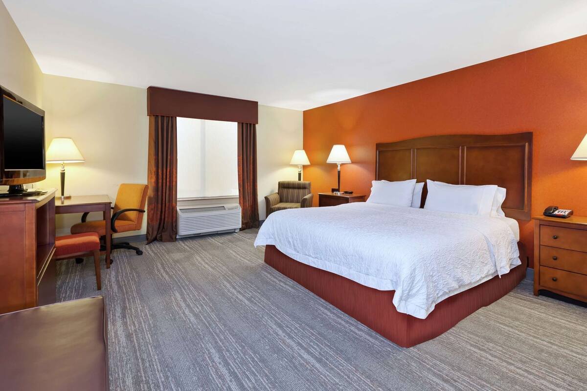 A hotel room with a large bed, a desk with a chair, a television, and a window with curtains.