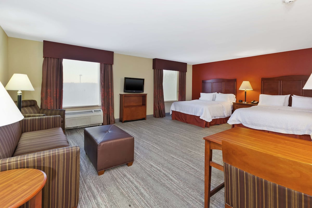 A hotel room with two beds, a sofa, a table, a TV, and a lamp.