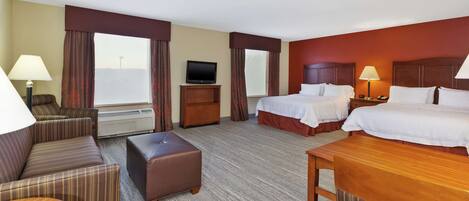 A hotel room with two beds, a sofa, a table, a TV, and a lamp.