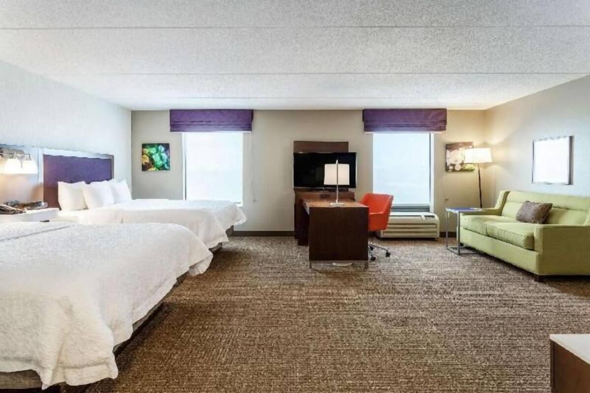 A hotel room with two beds, a desk, a chair, a sofa, and a TV.