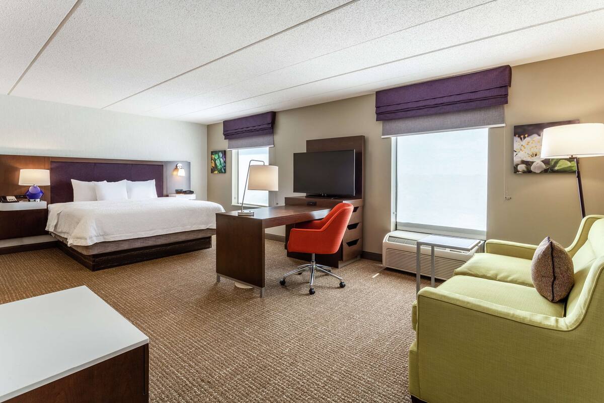 A hotel room with a bed, desk, chair, and a sofa.