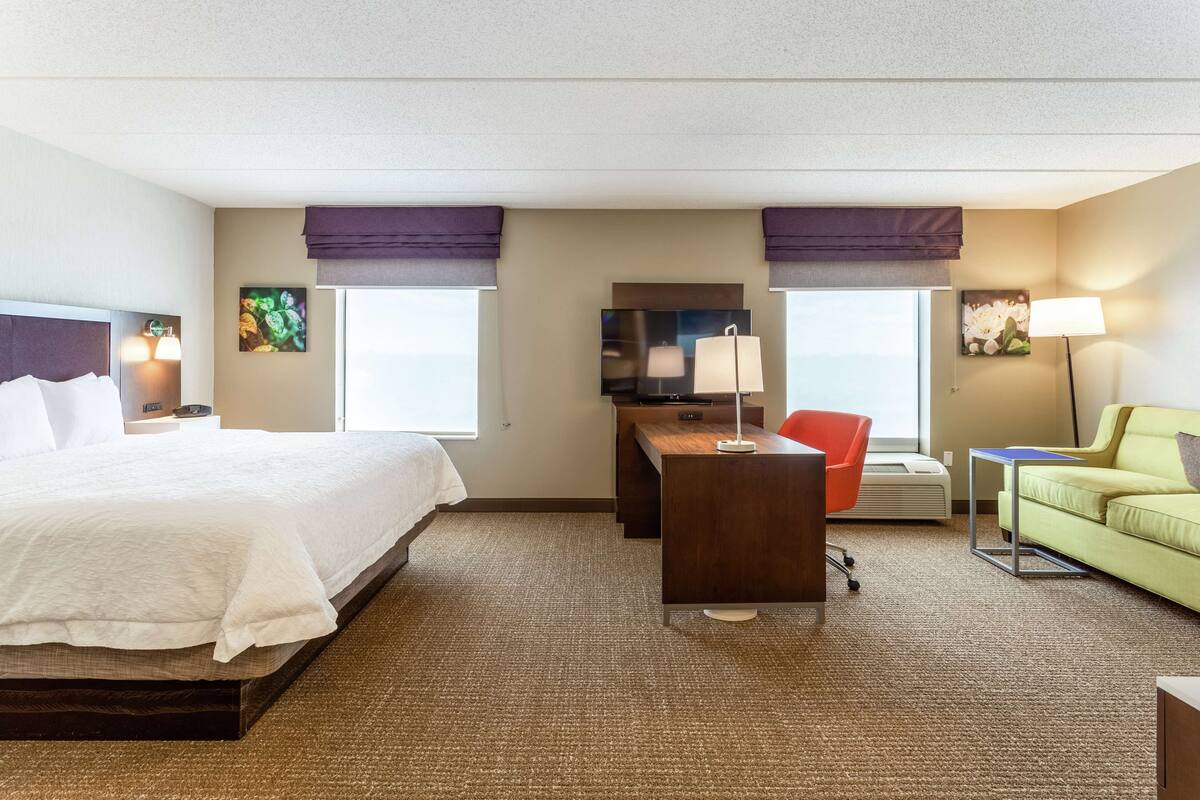 A hotel room with a bed, desk, two chairs, a sofa, and a TV.