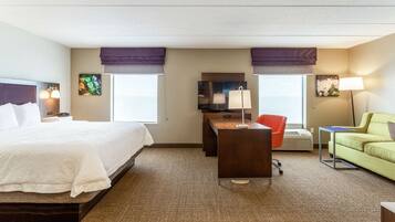 A hotel room with a bed, desk, two chairs, a sofa, and a TV.