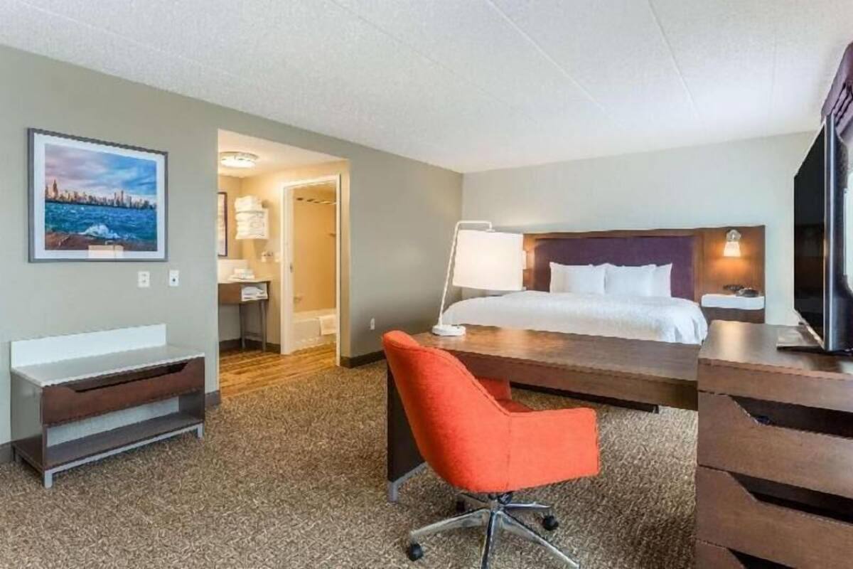 A hotel room with a bed, desk, chair, TV, and a painting on the wall.