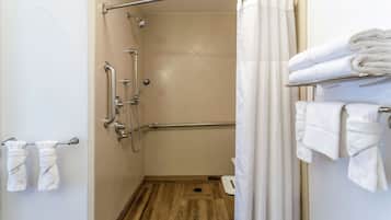 A shower area with a grab bar, a wooden floor, and a towel rack with towels.