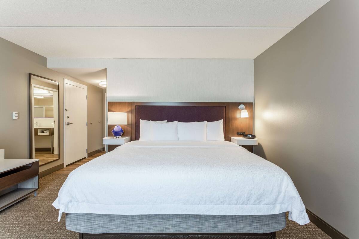 A hotel room with a large bed, bedside tables, a nightstand, a lamp, and a mirror.