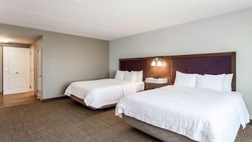 A hotel room with two beds, a nightstand, a lamp, and a door leading to another room.