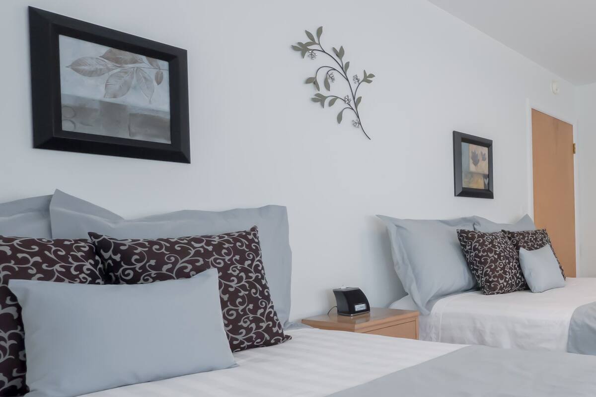 Hotellihuone, jossa on kaksi sänkyä, ja jokaisessa sängyssä on kuviollisia tyynyjä sekä seinällä kehystetty taulu.