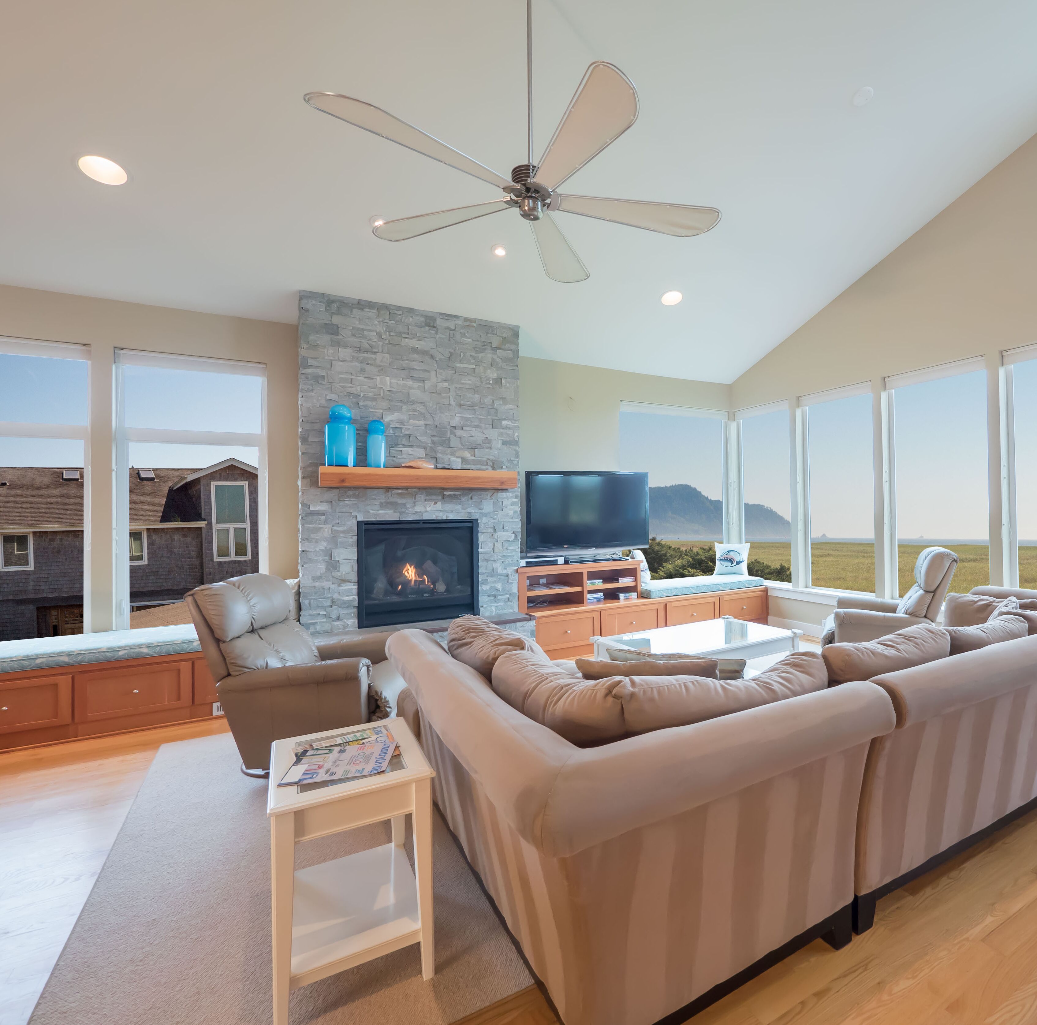 A modern living room with a stone fireplace, a large TV, and a ceiling fan.