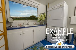 A kitchen with a large window, white cabinets, a sink, and a washing machine. - Seaside Vacation Homes (Seaside)