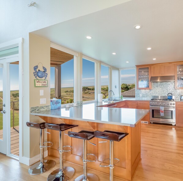 A modern kitchen with a large island, bar stools, and a view of the outdoors. - Seaside Vacation Homes (Seaside)