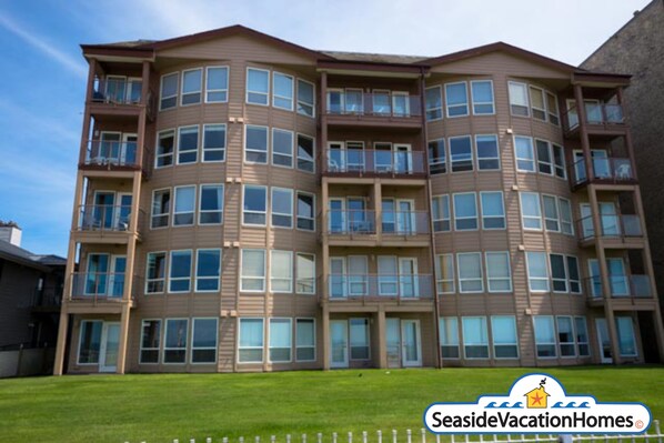 A multi-story residential building with balconies, large windows, and a grassy front yard. - Seaside Vacation Homes (Seaside)