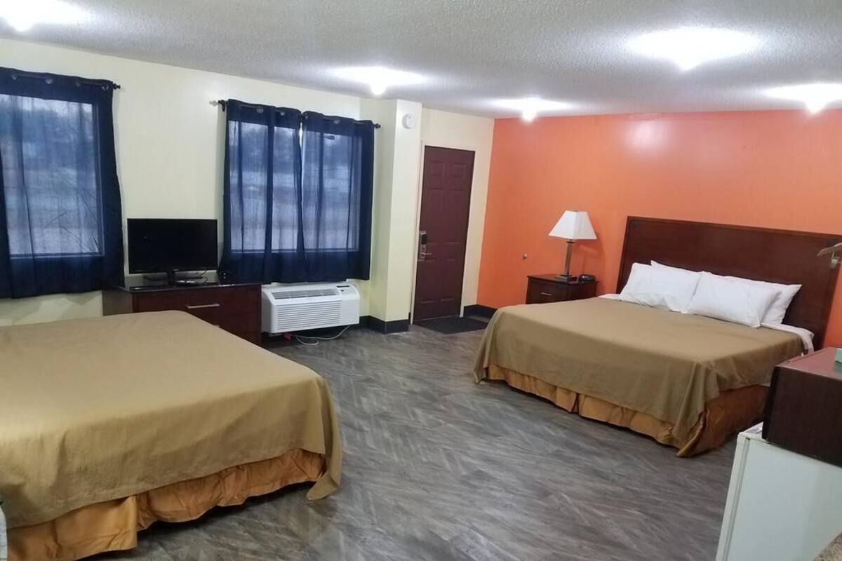 A hotel room with two beds, a TV, an air conditioner, a desk, and a lamp.