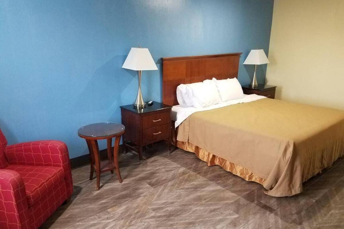 A hotel room with a bed, two bedside tables with lamps, a small round table, and a red chair.