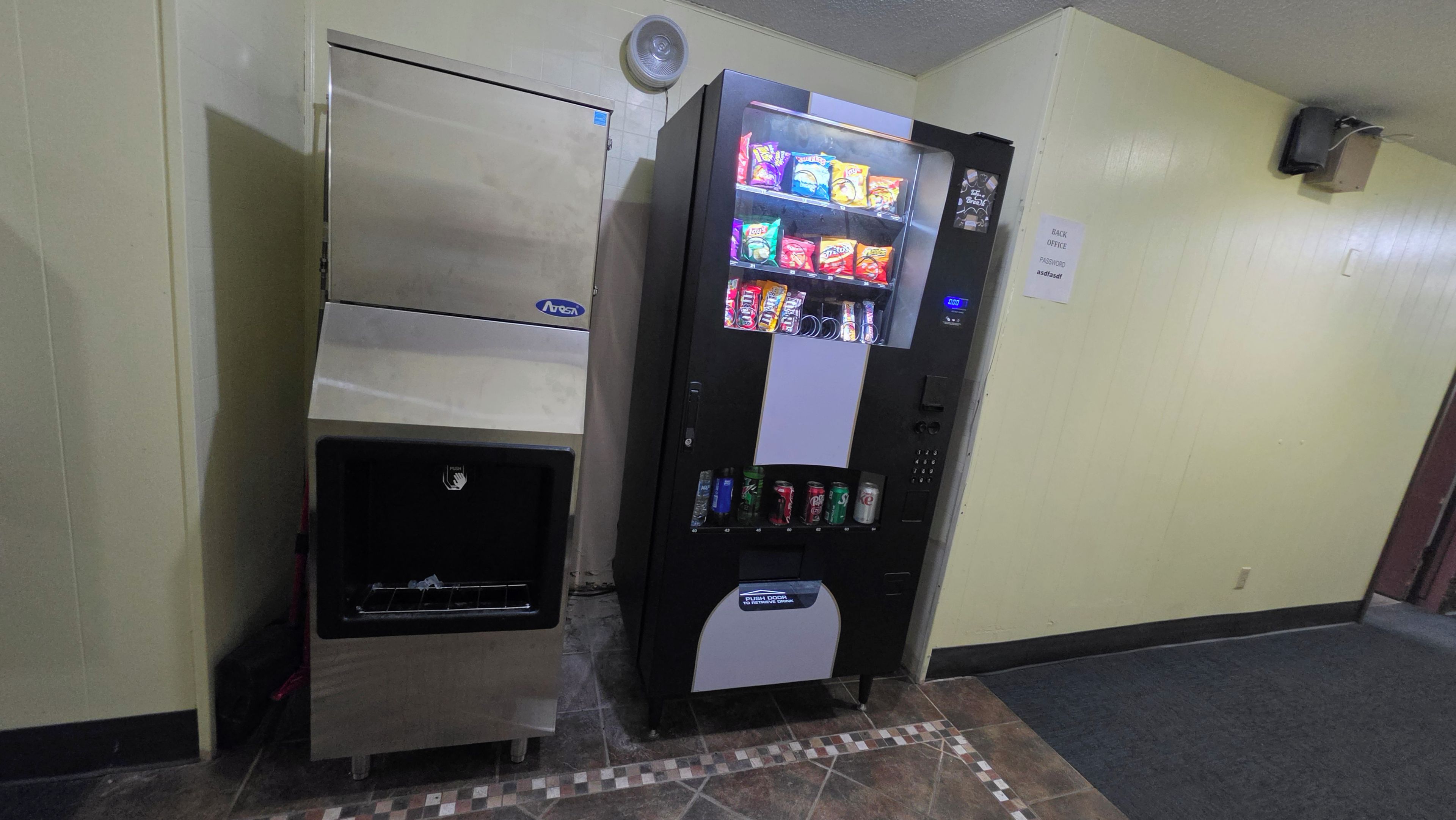 Máquina expendedora con aperitivos y bebidas, ranura para monedas y puerta de acceso para retirar los artículos.