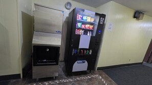 A vending machine with snacks and drinks, a coin slot, and a push door for retrieving items. - Western Inn South (Kearney)