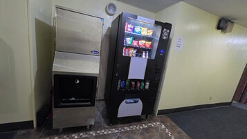 Máquina expendedora con aperitivos y bebidas, ranura para monedas y puerta de acceso para retirar los artículos.