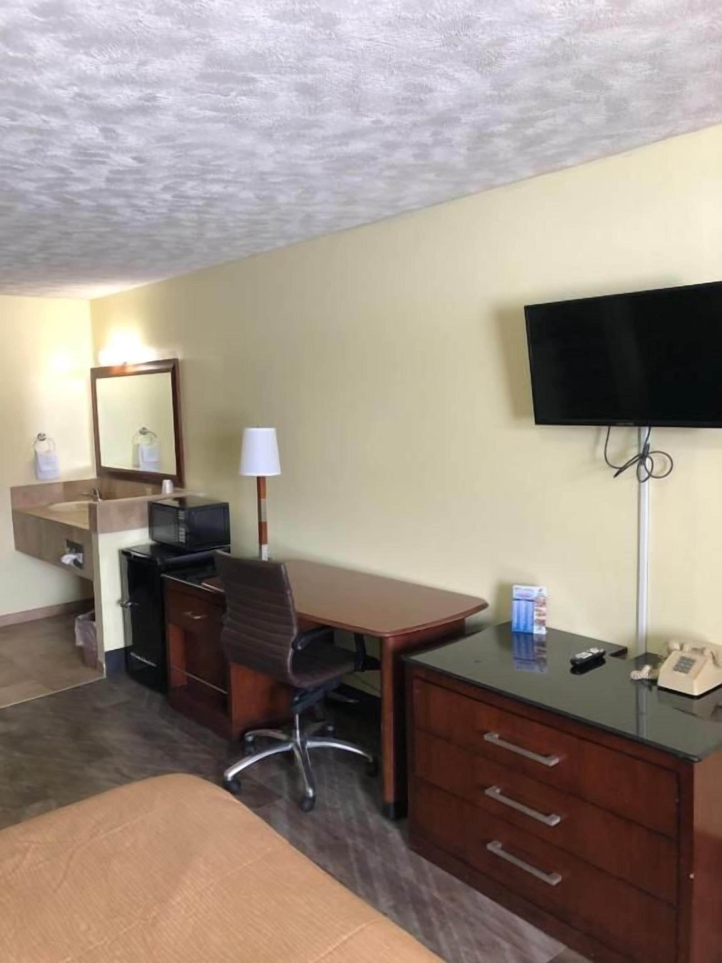 A hotel room with a bed, a desk, a chair, a television, a telephone, and a mirror.