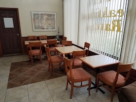Un comedor con mesas y sillas de madera, una puerta, una obra de arte enmarcada y una ventana con persianas.
