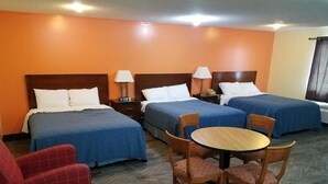 A hotel room with three beds, a round wooden table with chairs, and a red armchair. - Western Inn South (Kearney)
