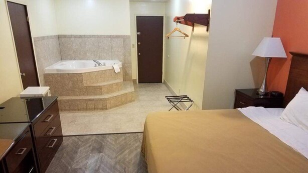 A hotel room with a bed, a bathroom with a bathtub, a desk, and a hanging clothes rack. - Western Inn South (Kearney)