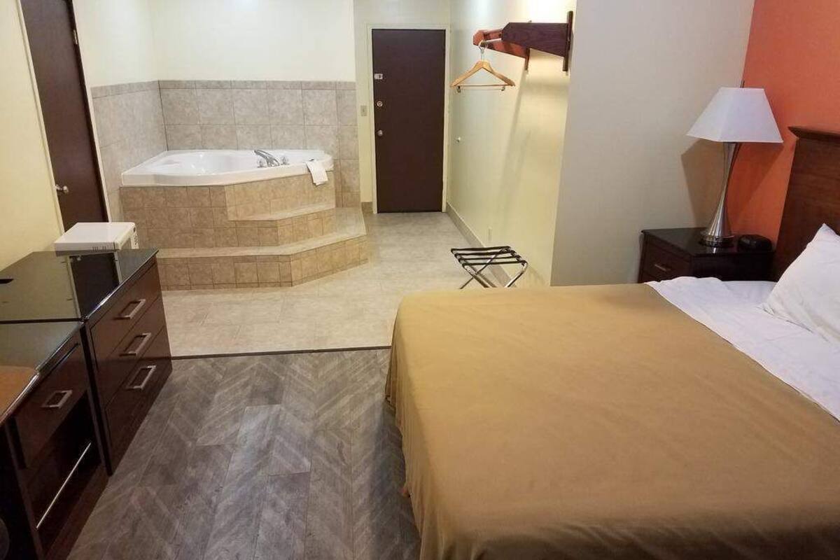 A hotel room with a bed, a bathroom with a bathtub, a desk, and a hanging clothes rack.