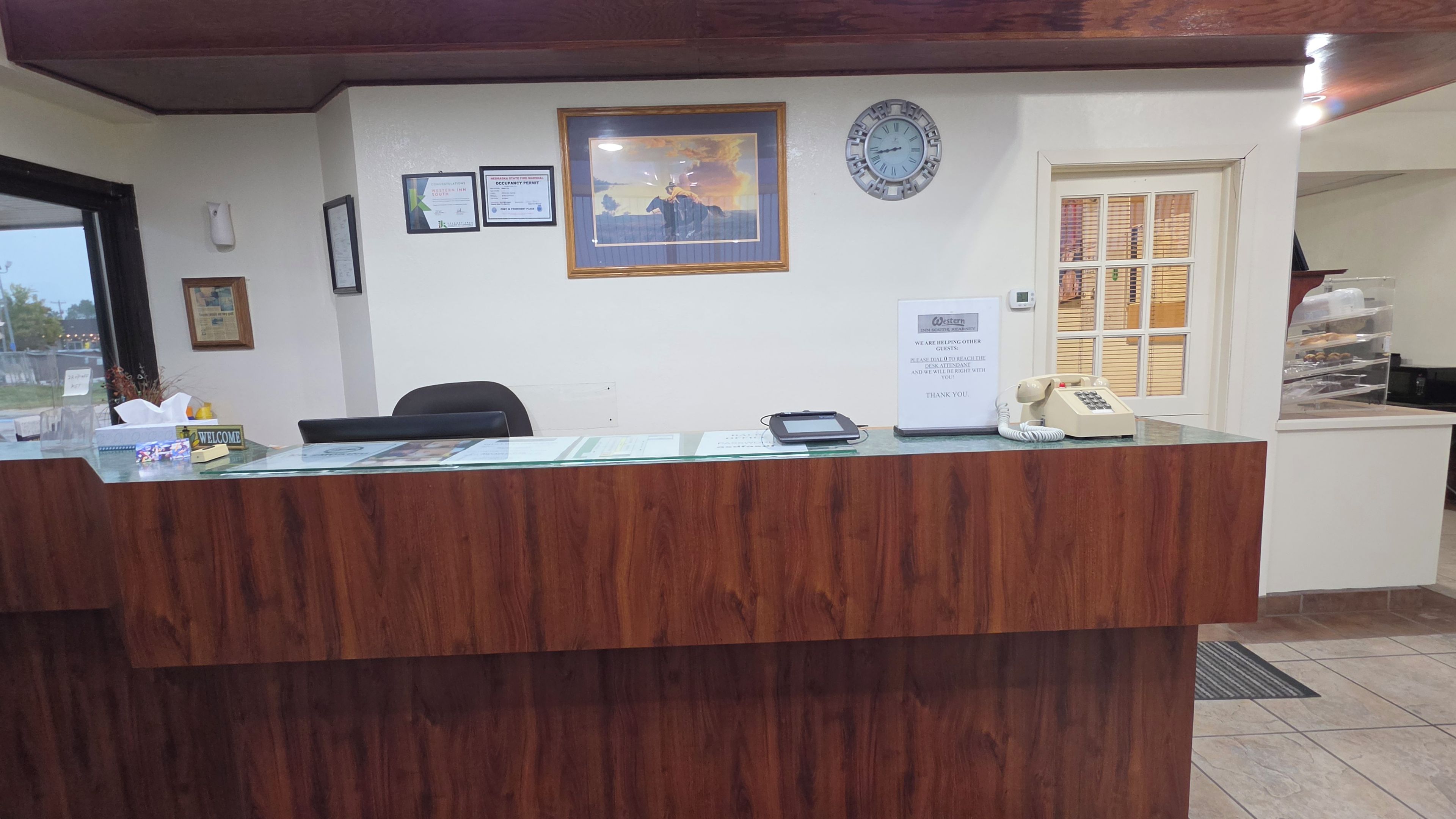 A reception desk with a clock, framed certificates, and a sign offering assistance to guests.