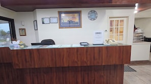 A reception desk with a clock, framed certificates, and a sign offering assistance to guests.