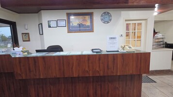 Mostrador de recepción con un reloj, diplomas enmarcados y un cartel ofreciendo asistencia a los huéspedes.