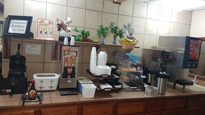 A breakfast counter with a waffle maker, a coffee machine, and a juice dispenser. - Western Inn South (Kearney)