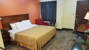 A hotel room with a bed, a chair, a desk, and a door. - Western Inn South (Kearney)
