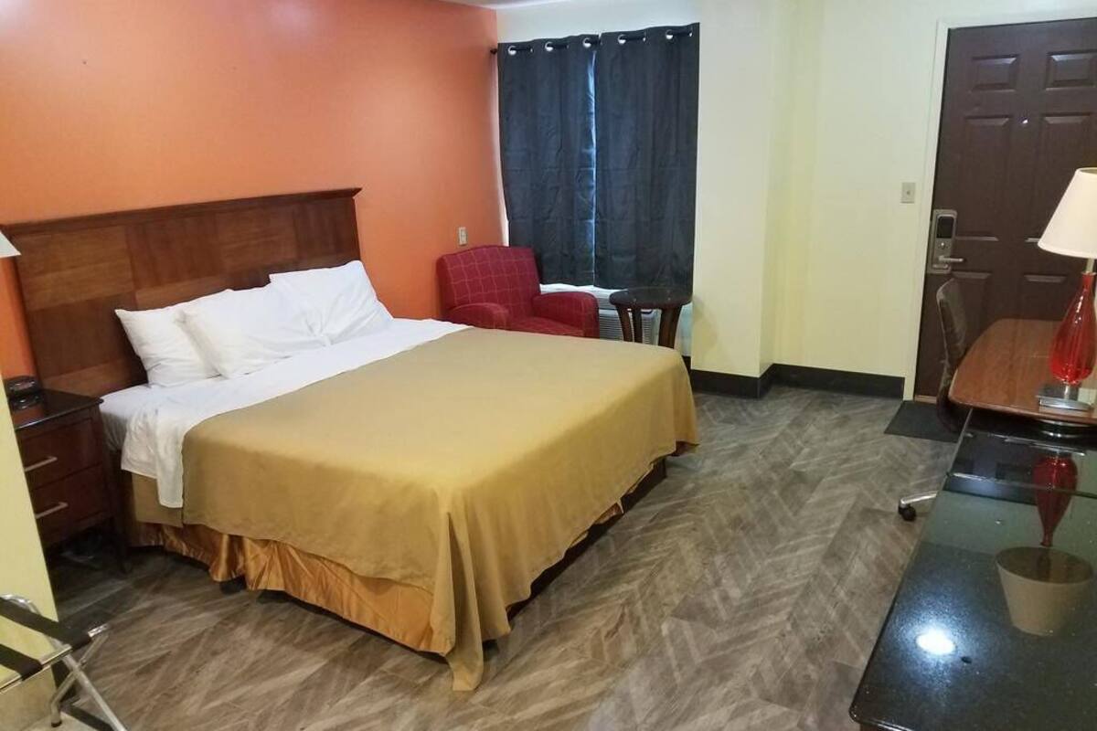 A hotel room with a bed, a chair, a desk, and a door.