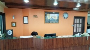A reception desk with a wooden counter, a clock, framed certificates, and a welcome sign. - Western Inn South (Kearney)