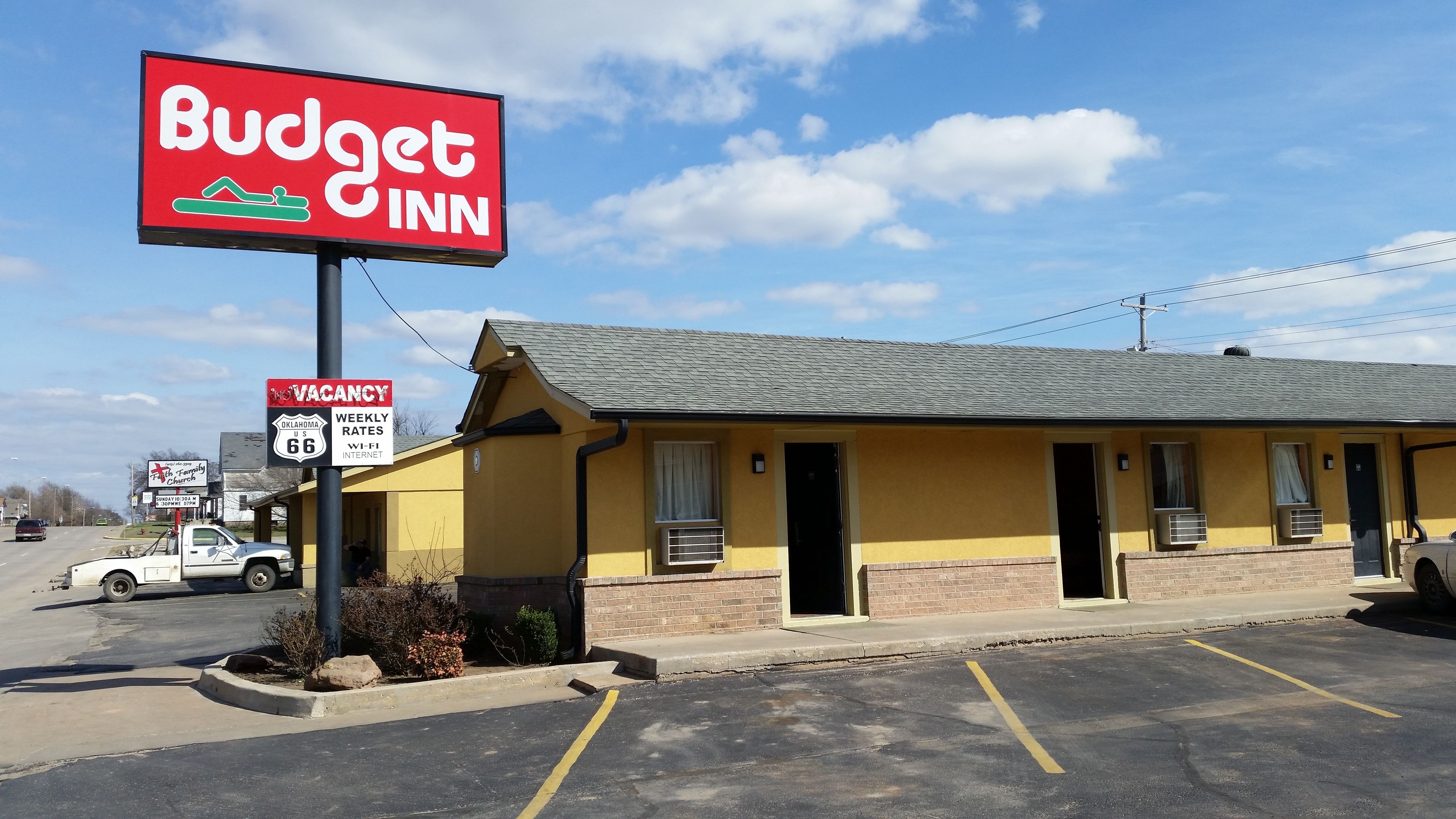 A Budget Inn with a vacant sign, a parking lot, and a church sign in the background.