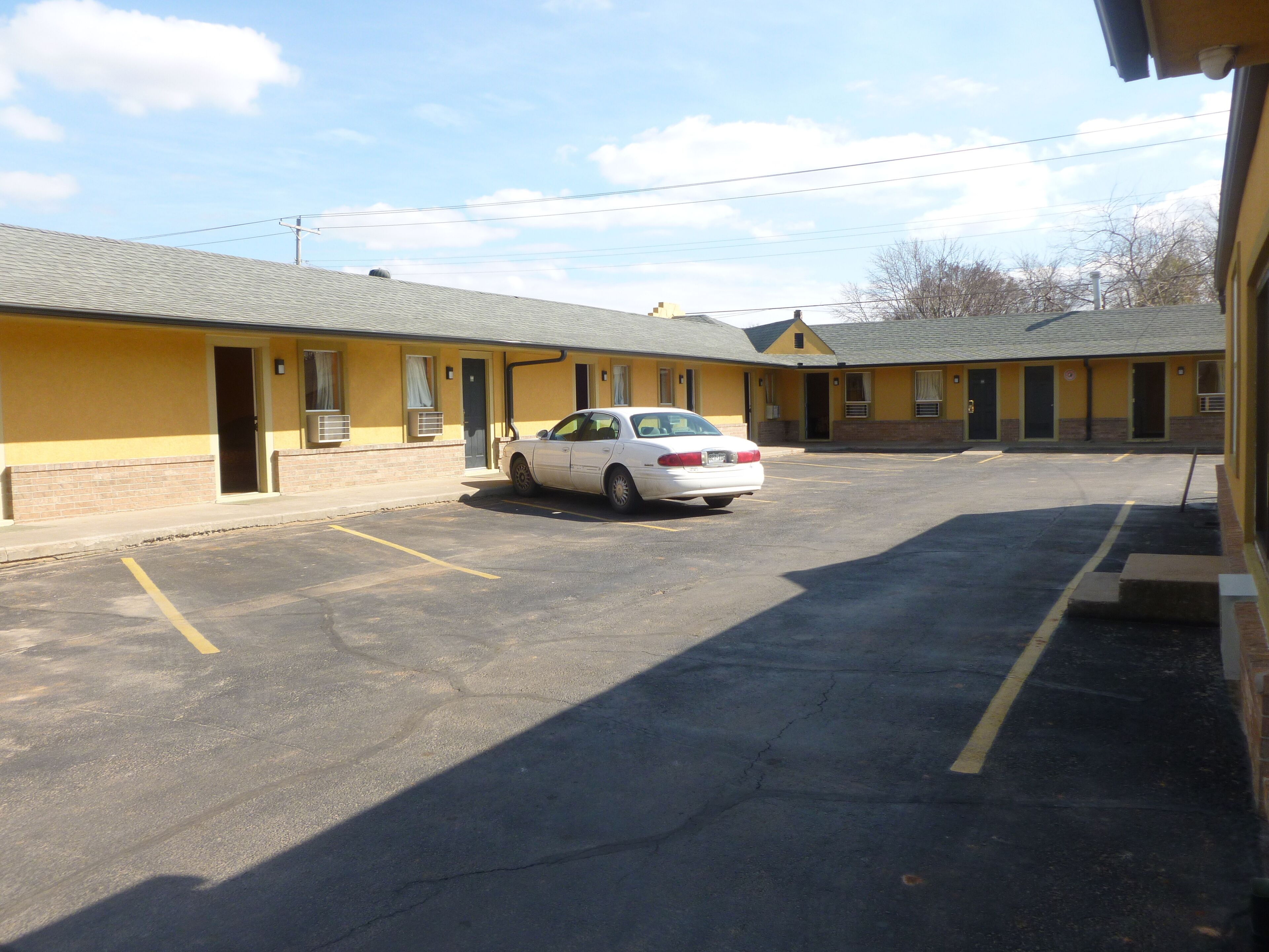 A parking lot with a white car parked in front of a yellow building with multiple doors and windows.