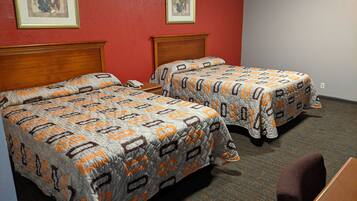 A hotel room with two beds, each with a patterned bedspread, wooden headboards, and a telephone on the nightstand.