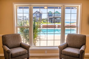 A room with two armchairs facing a large window with a view of a beach and houses. - Colonial Inn Motel (Nags Head)