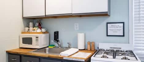 Una cocina con armarios blancos, un microondas, un fregadero, una estufa y un letrero de bienvenida.