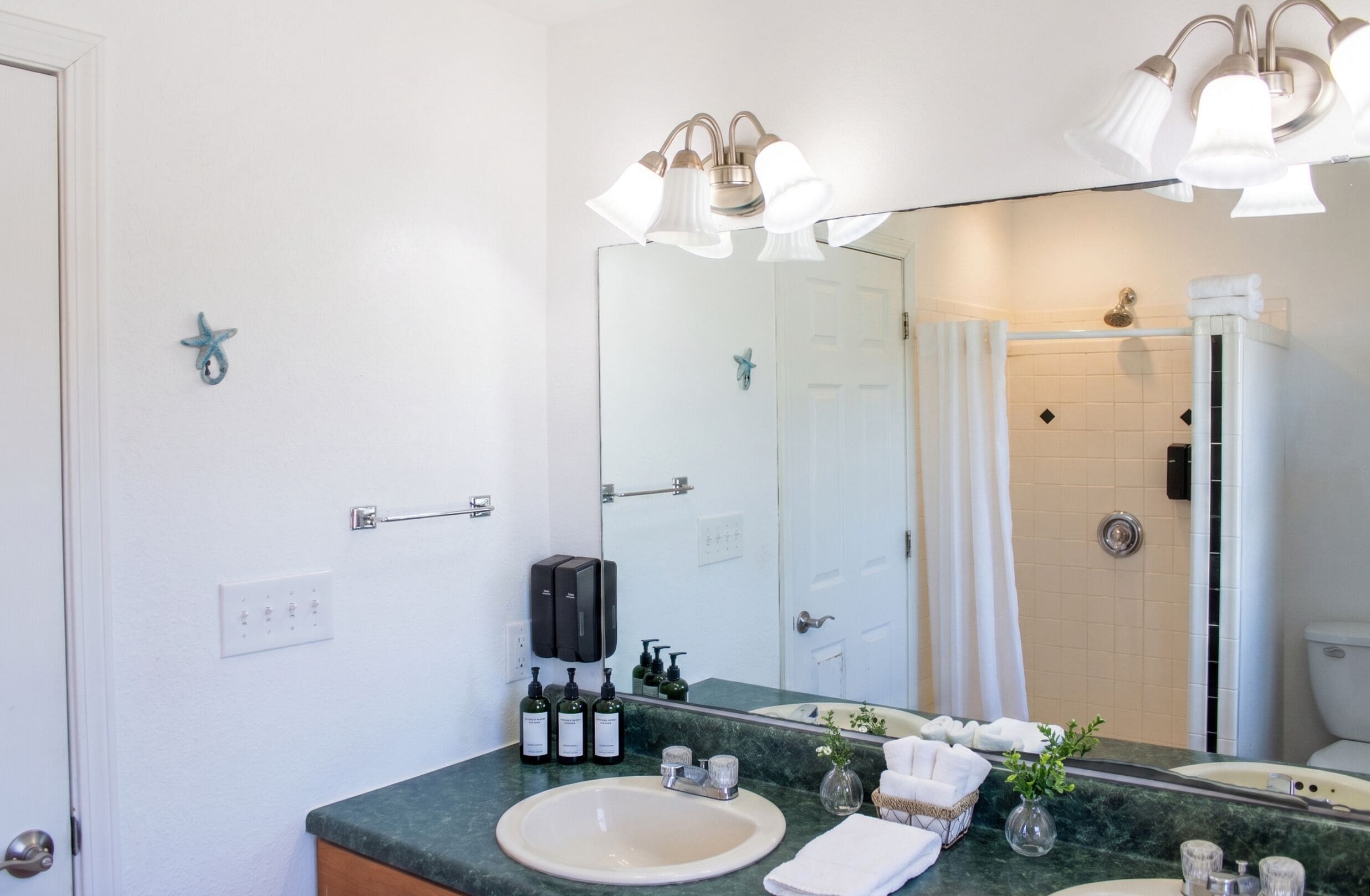 A bathroom with a sink, mirror, shower, and towel rack.