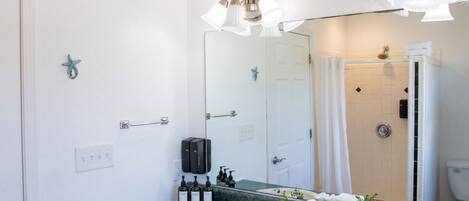 A bathroom with a sink, mirror, shower, and towel rack.