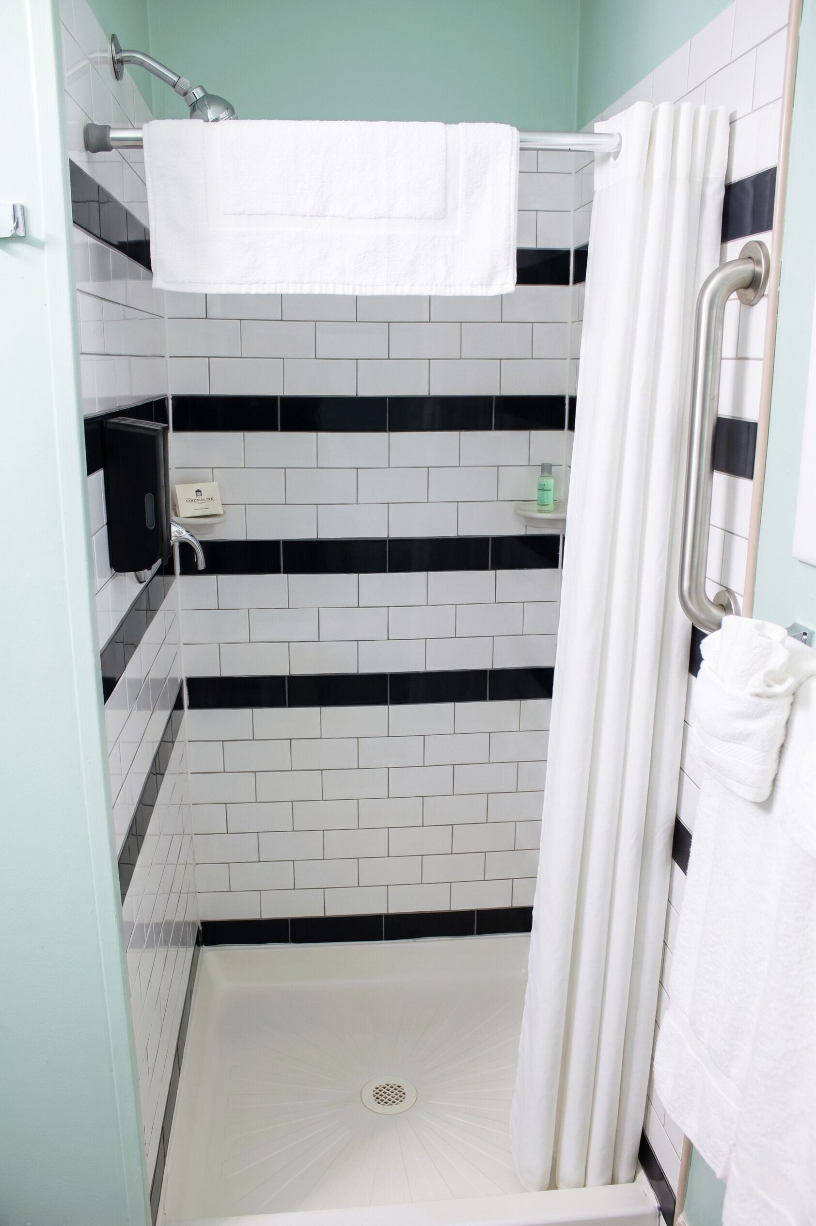A shower with a white towel, a handrail, and a tiled wall with black and white patterns.