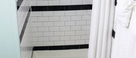 A shower with a white towel, a handrail, and a tiled wall with black and white patterns.