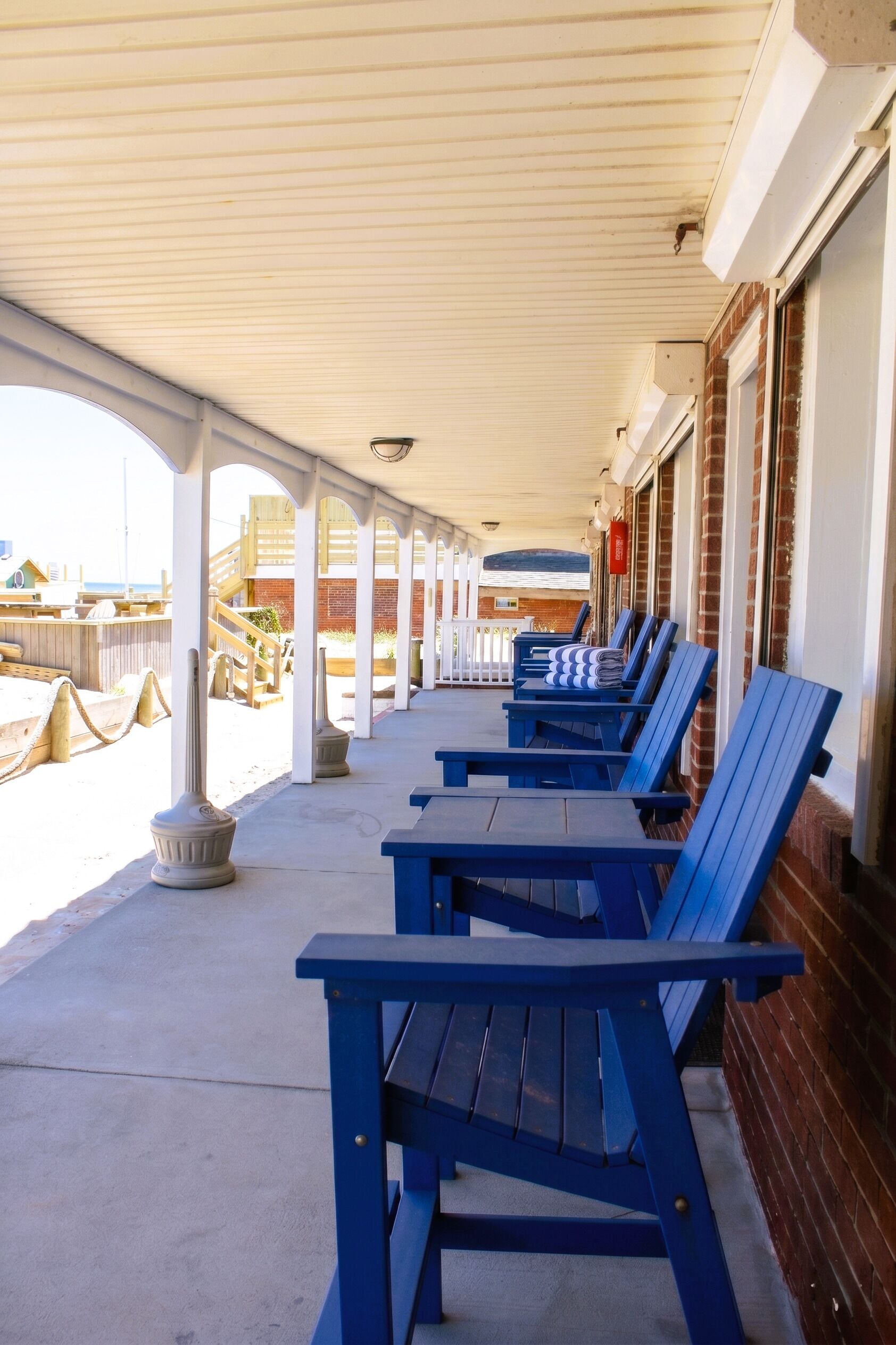 A covered outdoor seating area with blue chairs and a concrete floor.