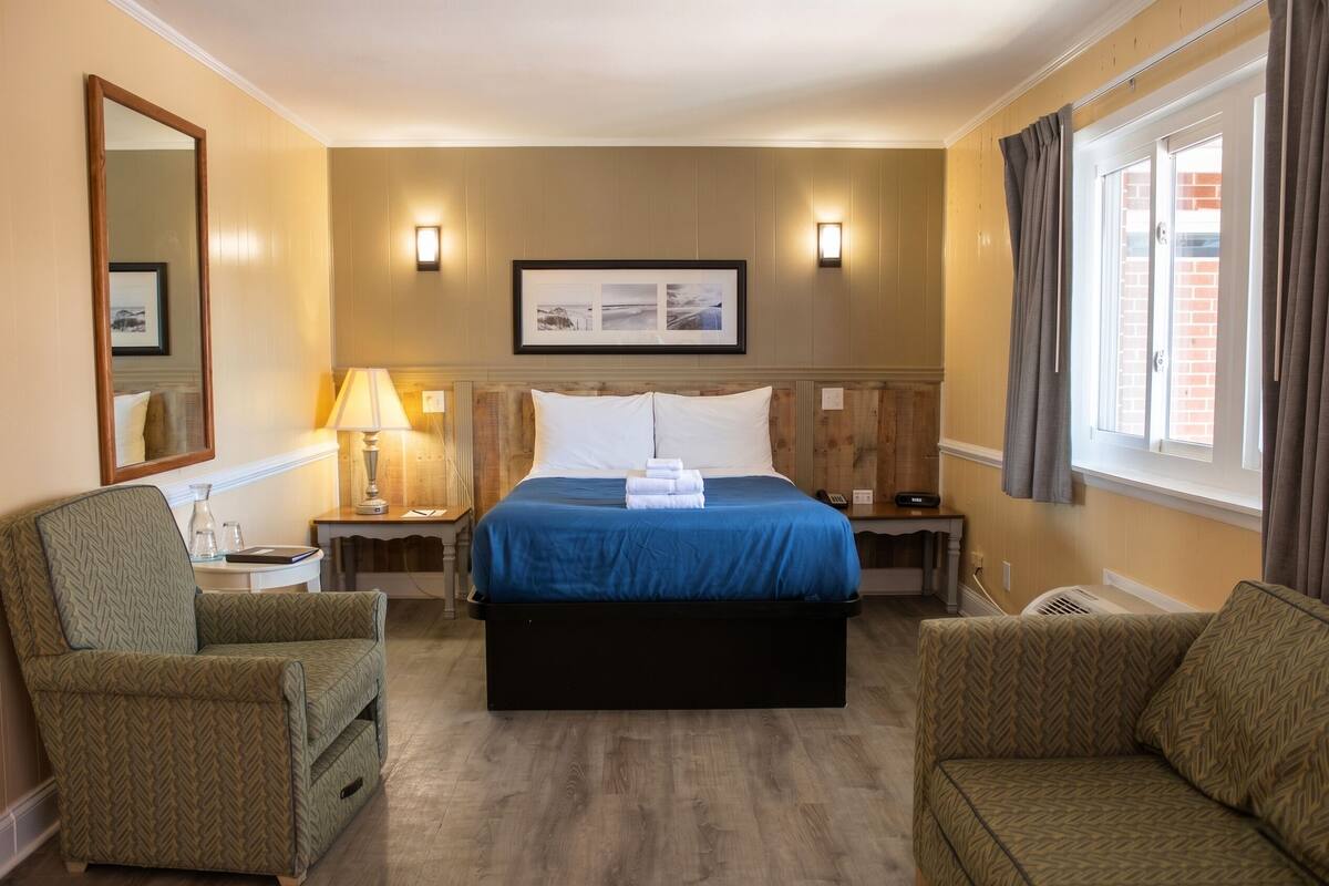 A hotel room with a bed, two bedside tables, a chair, a sofa, a mirror, and a window with curtains.