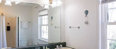 Un baño con un espejo grande, dos lavamanos y una ducha.