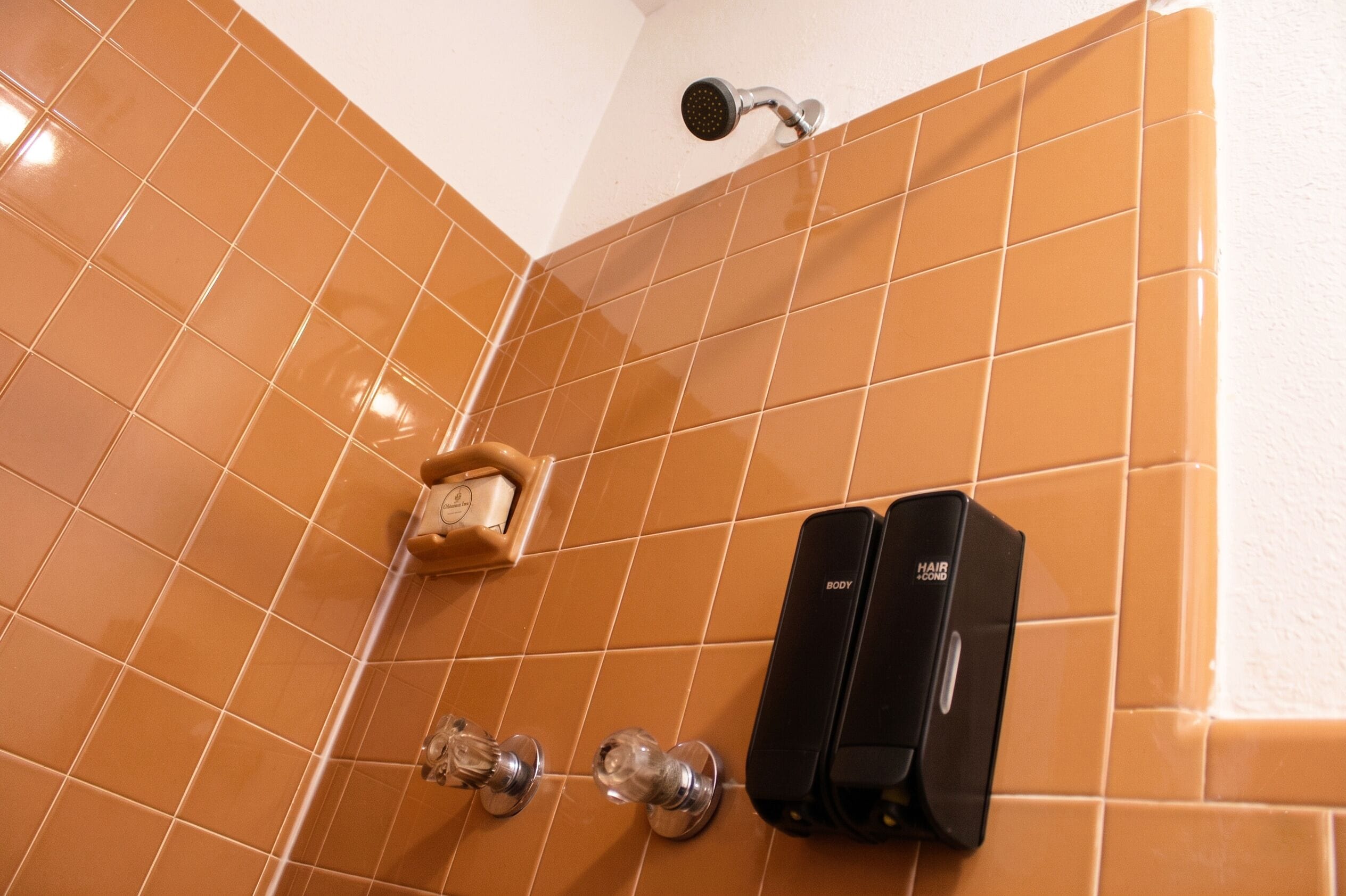 A bathroom with orange tiles, a showerhead, a soap dispenser, and a hair dryer.