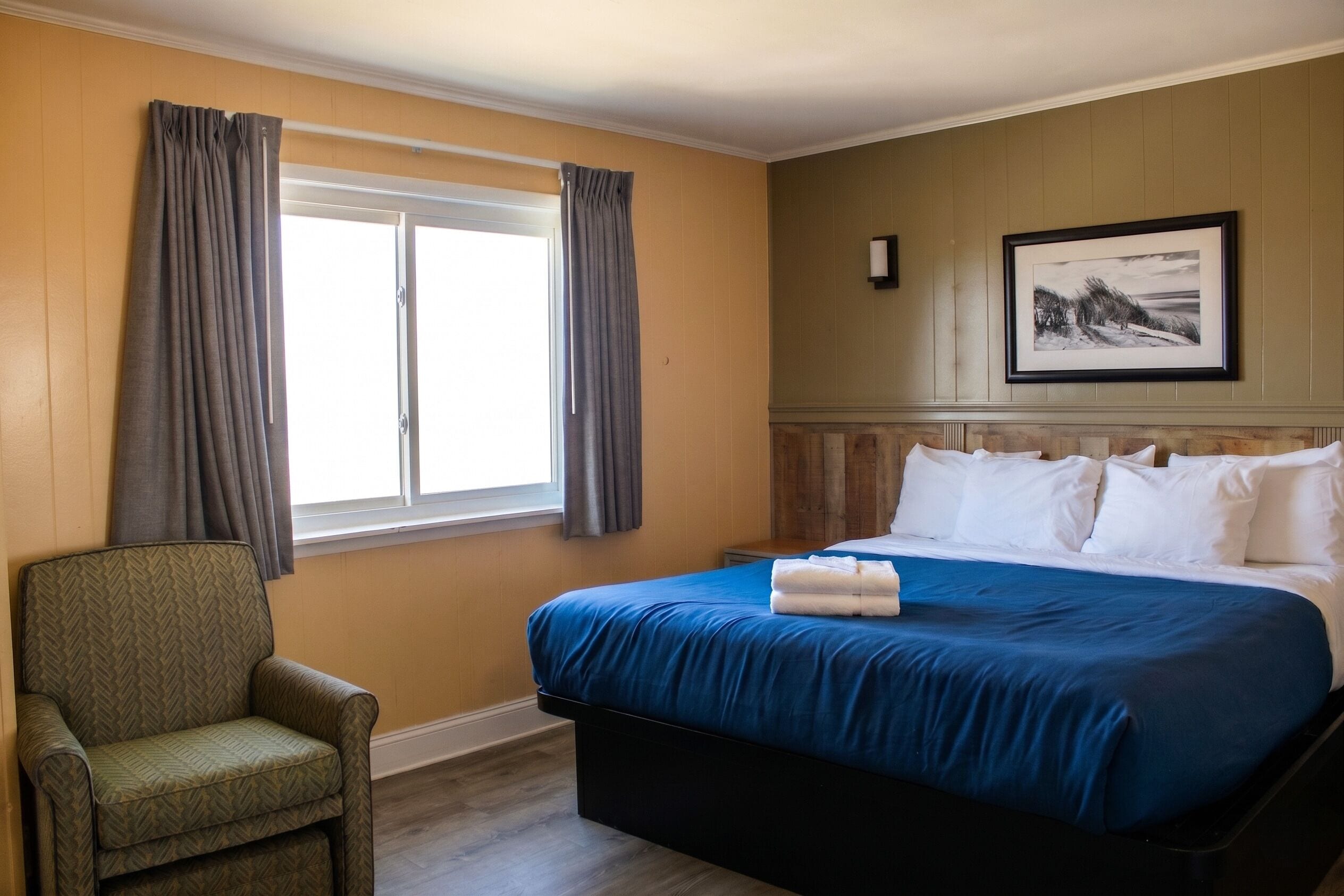 Habitación de hotel con cama, una silla, ventana con cortinas, un cuadro en la pared y una chimenea.